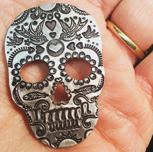 Ornate hand stamped Day of the Dead skull in the palm of a hand.